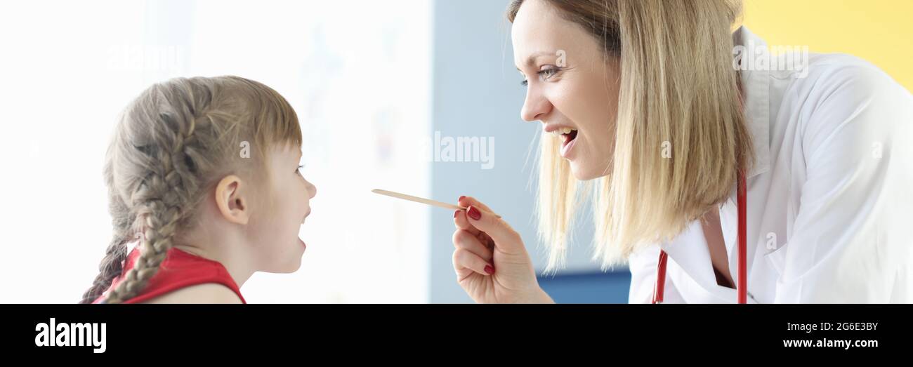 Femme médecin examinant la gorge de la petite fille avec la spatule dedans clinique Banque D'Images