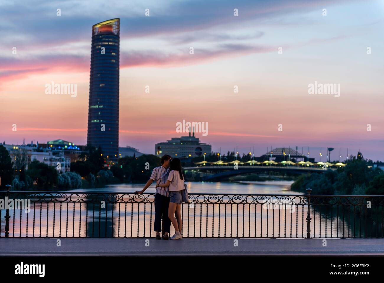 Couple debout sur le pont au coucher du soleil et embrassant, Puente de Triana, vue sur le fleuve Rio Guadalquivir, dans le gratte-ciel arrière Torre Sevilla Banque D'Images