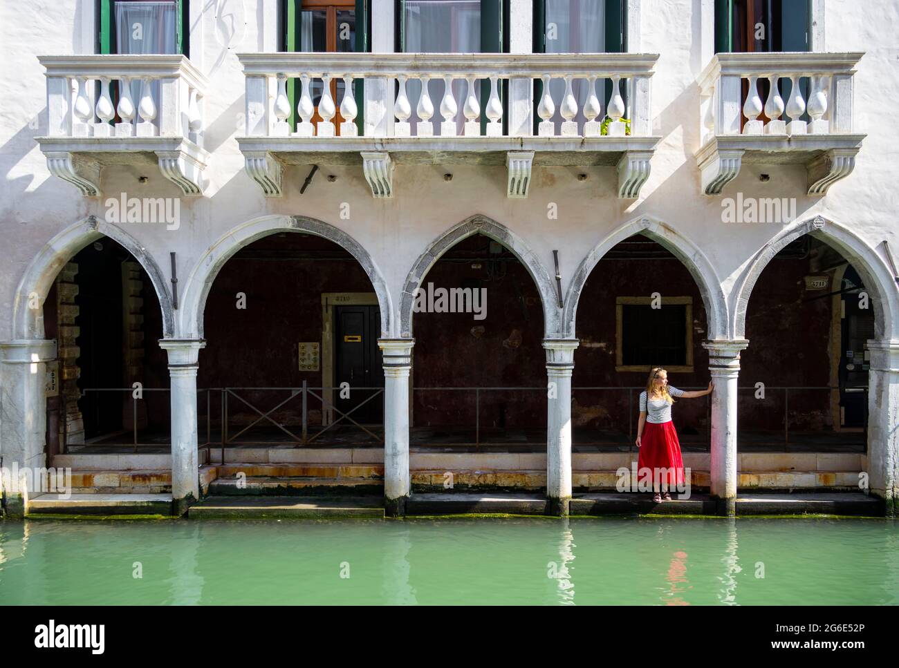 Jeune femme debout dans un portique près d'un canal, Venise, Vénétie, Italie Banque D'Images