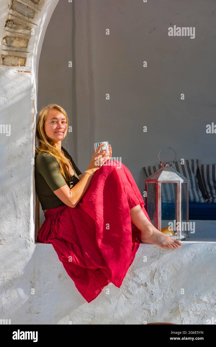 Jeune femme tenant une tasse et assise sur le mur, Grèce Banque D'Images