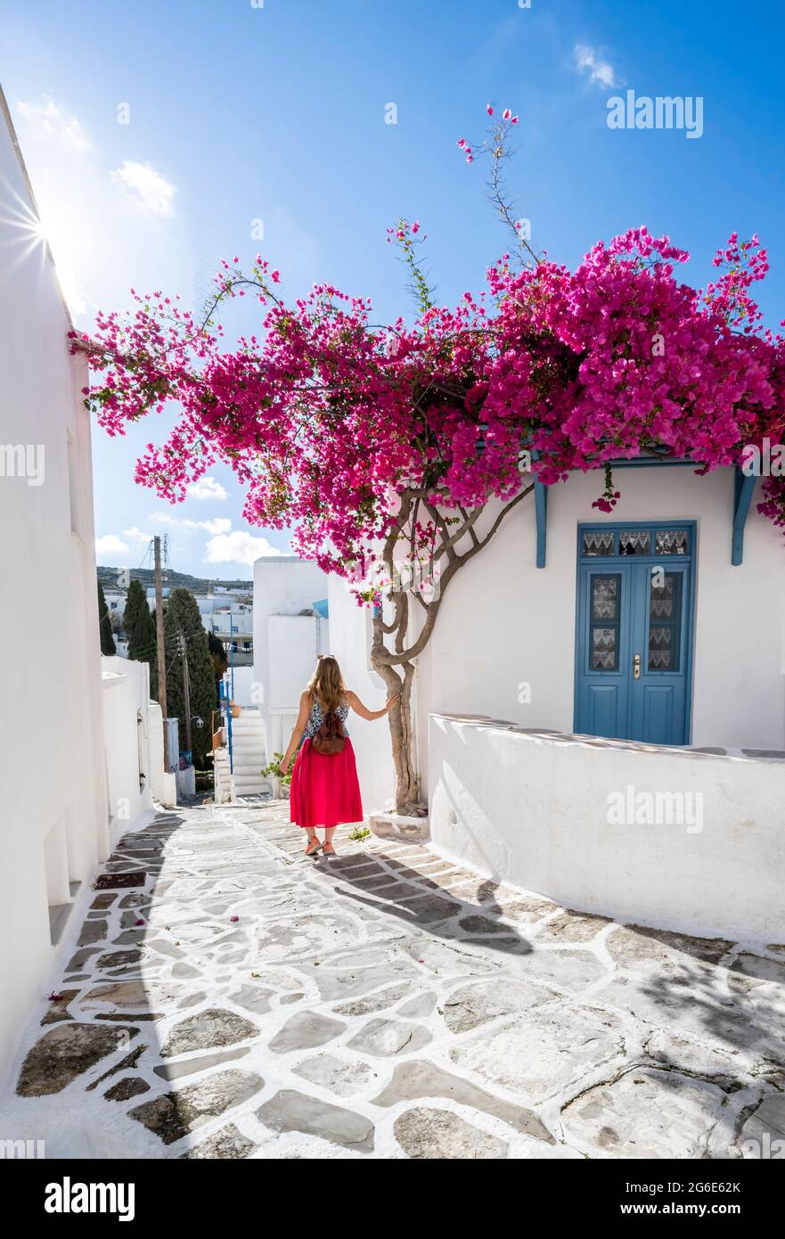 Maisons blanches-bleues avec bougainvillea pourpre en fleurs (Bougainvillea), Jeune femme à la robe rouge dans la vieille ville de Lefkes, Paros, Cyclades, Grèce Banque D'Images