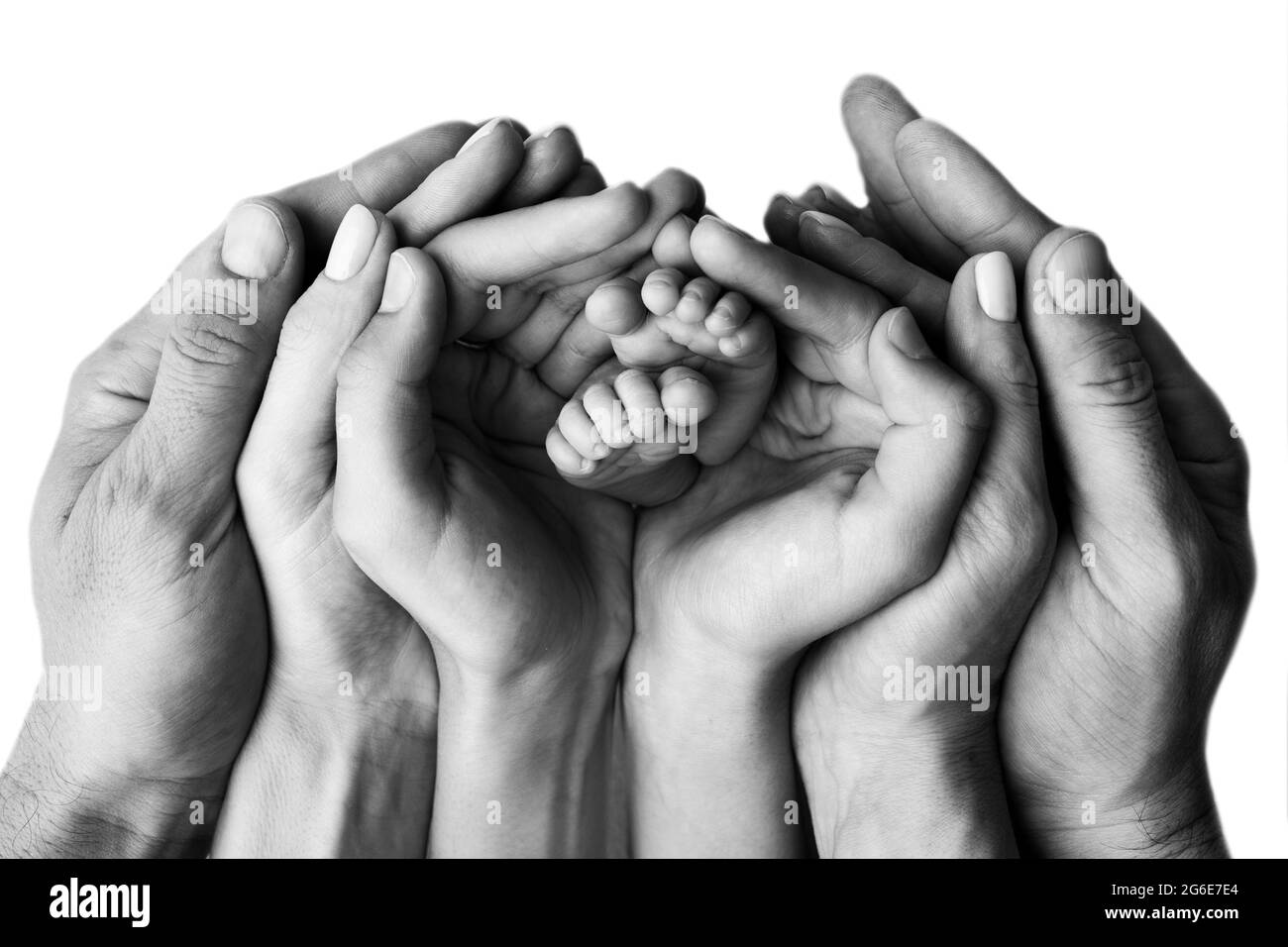Les mains de la mère, du père et de l'enfant plus âgé tiennent les pieds du nouveau-né. Joli portrait de famille avec bébé. Photographie en noir et blanc. Banque D'Images