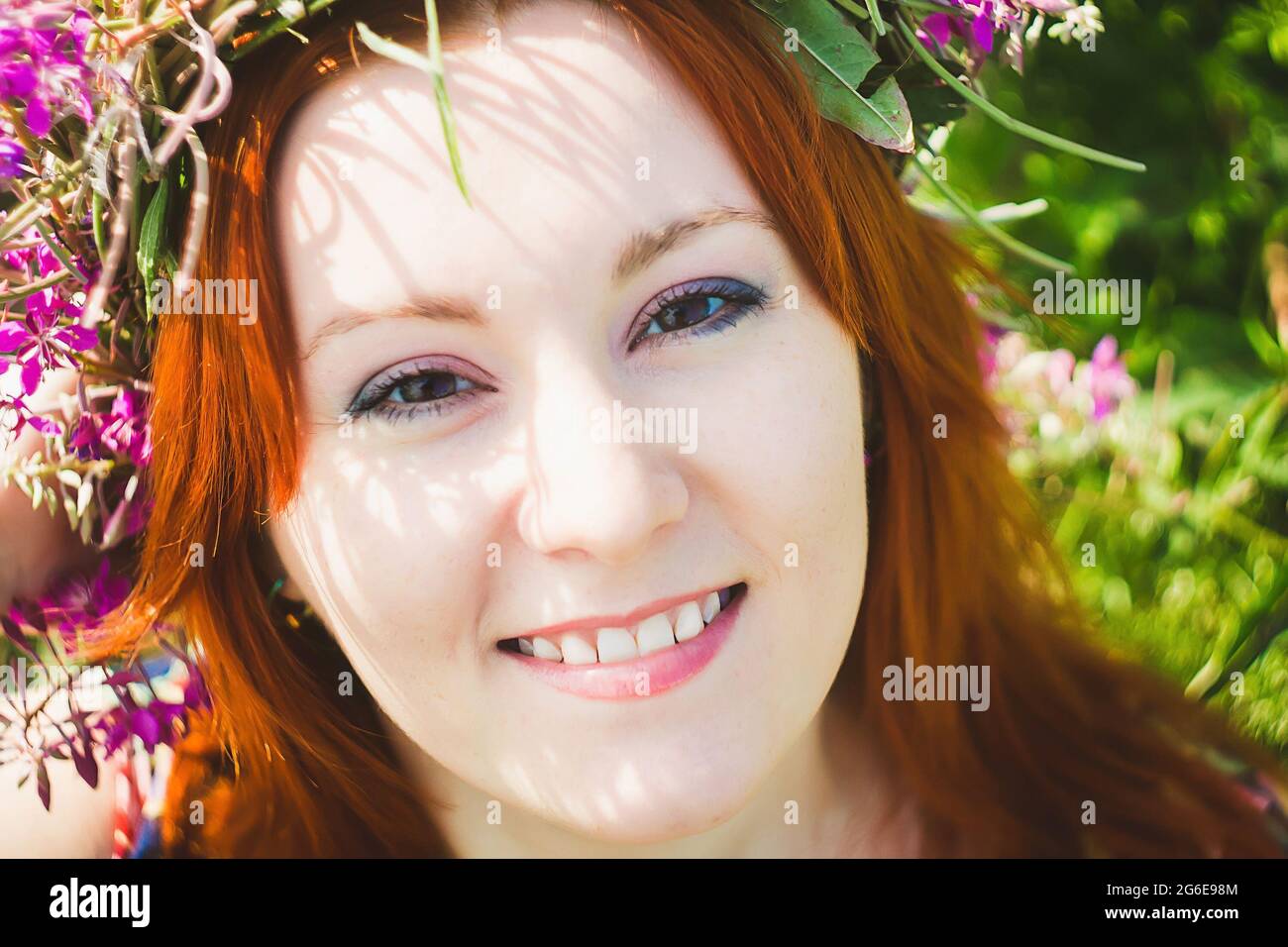 Portrait d'une jeune belle femme aux cheveux rouges avec une couronne de fleurs roses sur sa tête. Une femme attirante sourit. Style été Banque D'Images