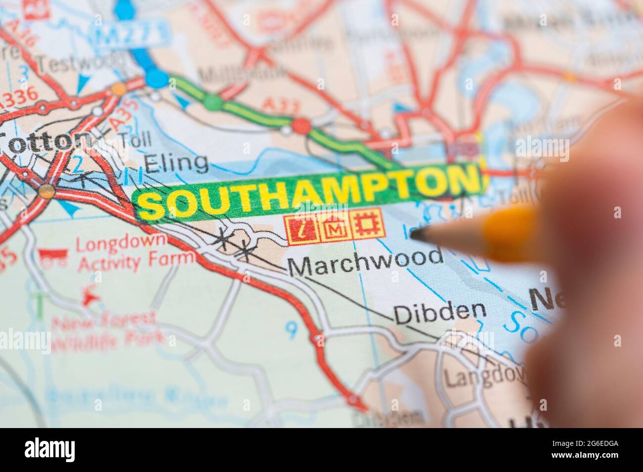 Gros plan d'une page sur une carte routière imprimée atlas avec la main d'un homme tenant un crayon pointant vers la ville de Southampton en Angleterre. Concept : lecture de cartes Banque D'Images