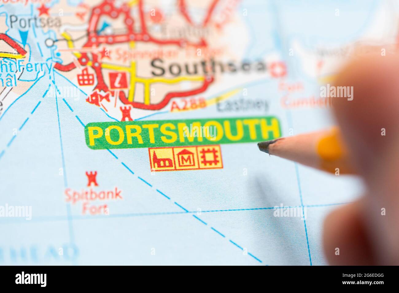 Gros plan d'une page sur une carte routière imprimée atlas avec la main d'un homme tenant un crayon pointant vers la ville de Portsmouth en Angleterre. Concept : lecture de cartes Banque D'Images