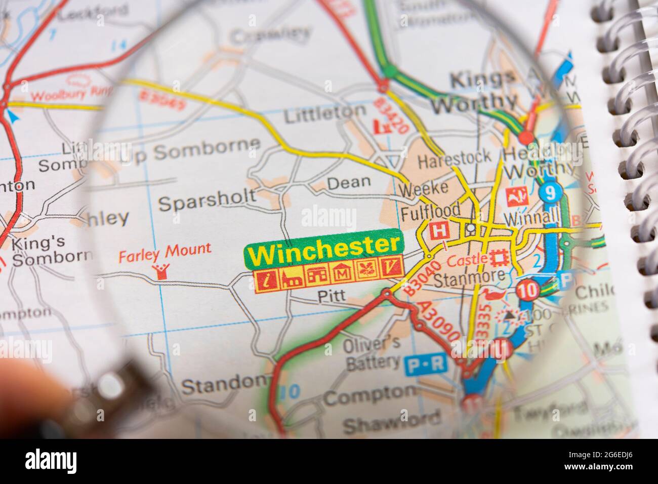 Gros plan d'une page sur une carte routière imprimée atlas avec la main d'un homme tenant une loupe montrant un agrandissement de la ville de Winchester en Angleterre Banque D'Images