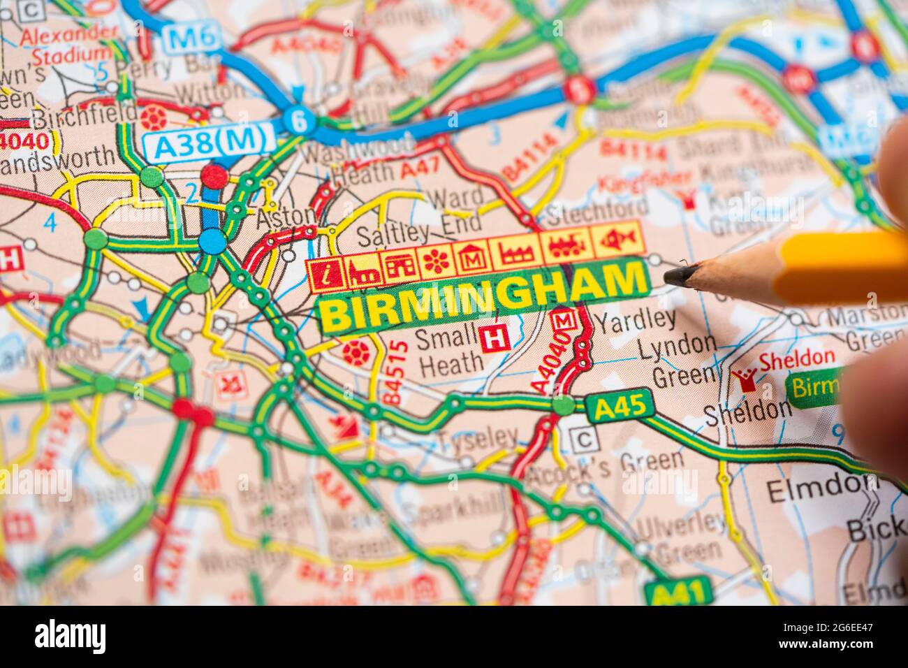 Gros plan macro d'une page sur une carte routière imprimée atlas avec la main d'un homme tenant un crayon pointant vers Birmingham, Angleterre. Concept : lecture de cartes Banque D'Images