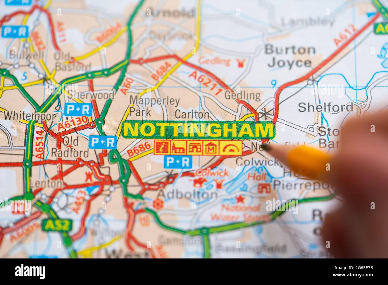Macro gros plan d'une page sur une carte routière imprimée atlas avec la main d'un homme tenant un crayon pointant à Nottingham, Angleterre. Concept : lecture de cartes Banque D'Images