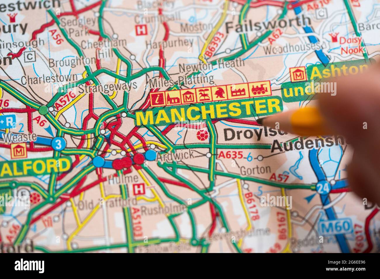 Gros plan macro d'une page sur une carte routière imprimée atlas avec la main d'un homme tenant un crayon pointant vers Manchester, Angleterre. Concept : lecture de cartes Banque D'Images