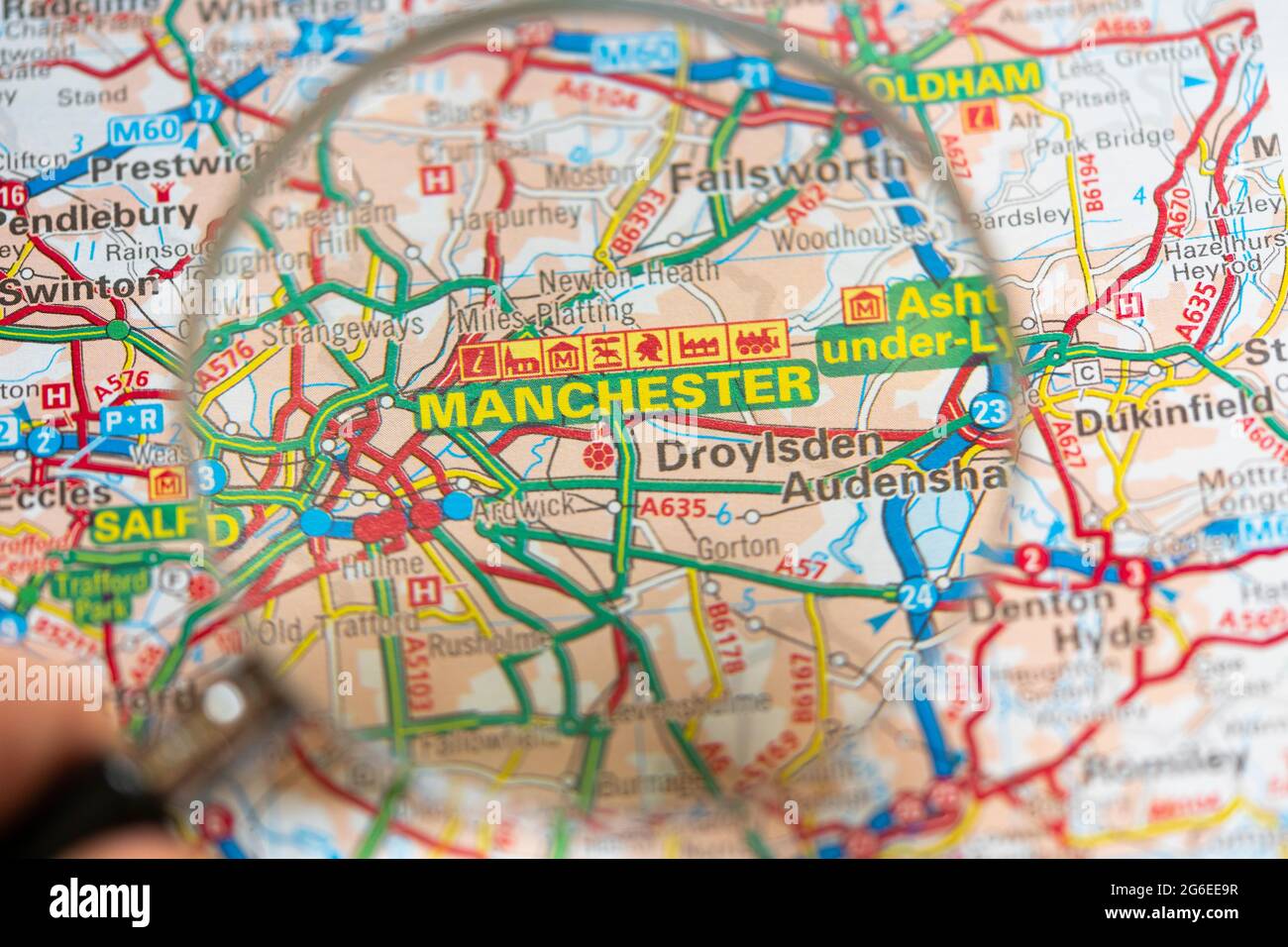 Macro gros plan d'une page sur une carte routière imprimée atlas avec la main d'un homme tenant une loupe montrant un agrandissement de Manchester, Angleterre Banque D'Images