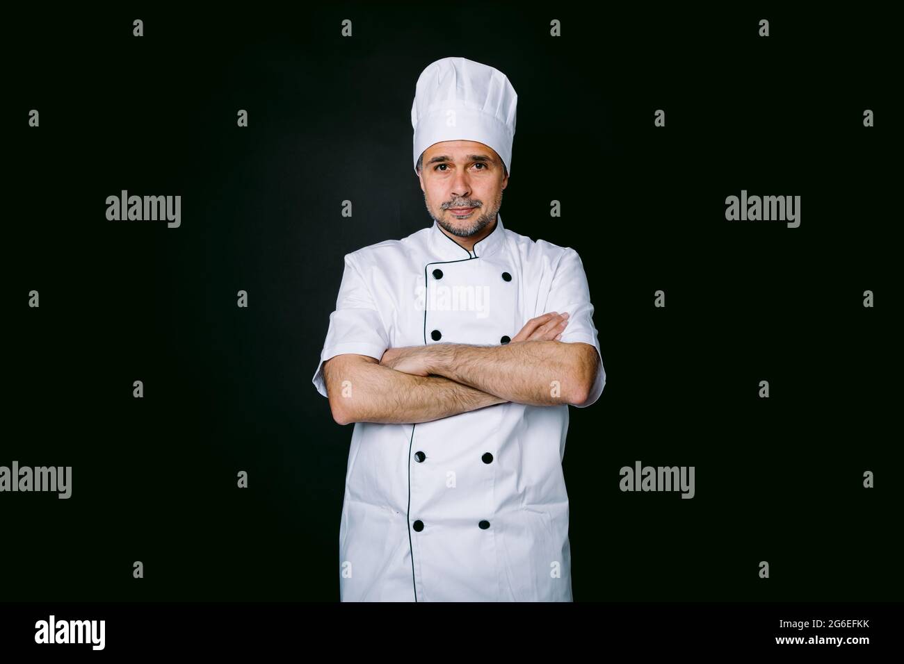 Chef cuisinier portant une veste et un chapeau de cuisine, bras croisés,  sur fond noir Photo Stock - Alamy