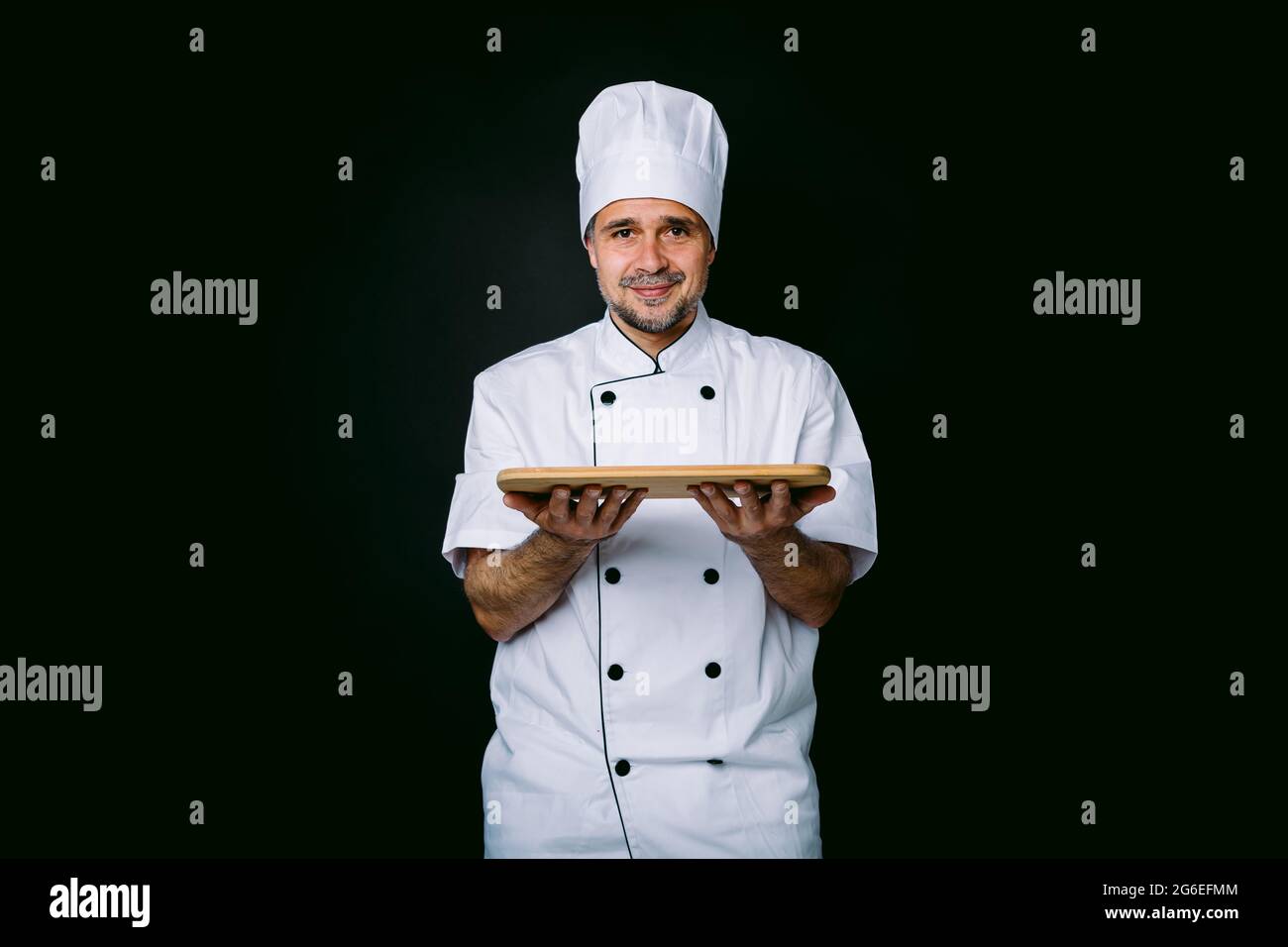 Chef cuisinier portant une veste et un chapeau de cuisine, tenant un  plateau en bois, sur fond noir Photo Stock - Alamy