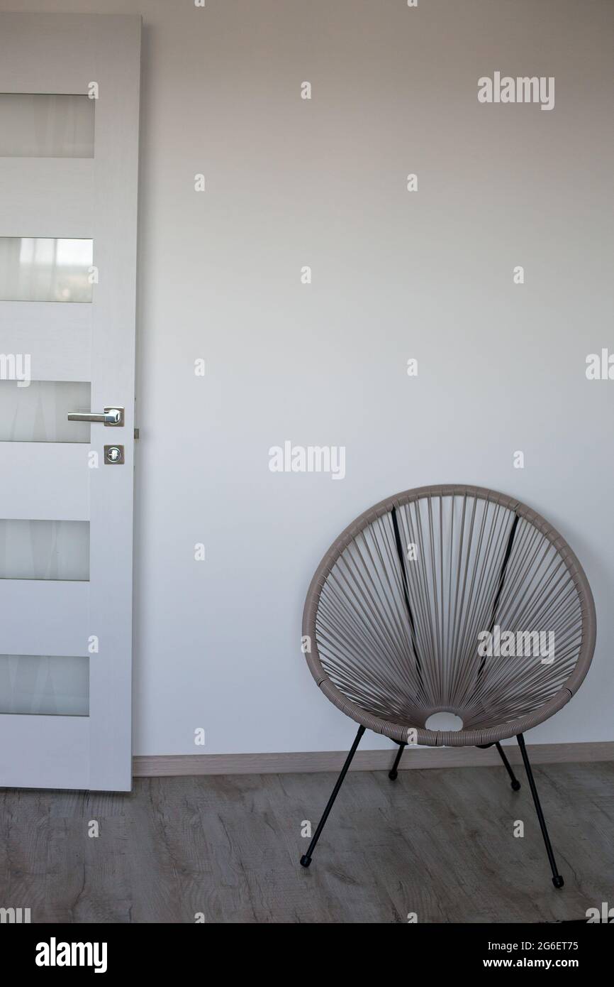 Partie de la chambre avec une chaise cappuccino, mur blanc, sol gris et porte blanche Banque D'Images