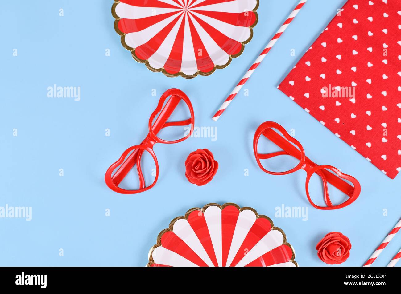 Plat de fête avec assiettes en papier, verres en forme de coeur, roses, confetti et pailles à boire sur fond bleu avec espace de copie Banque D'Images