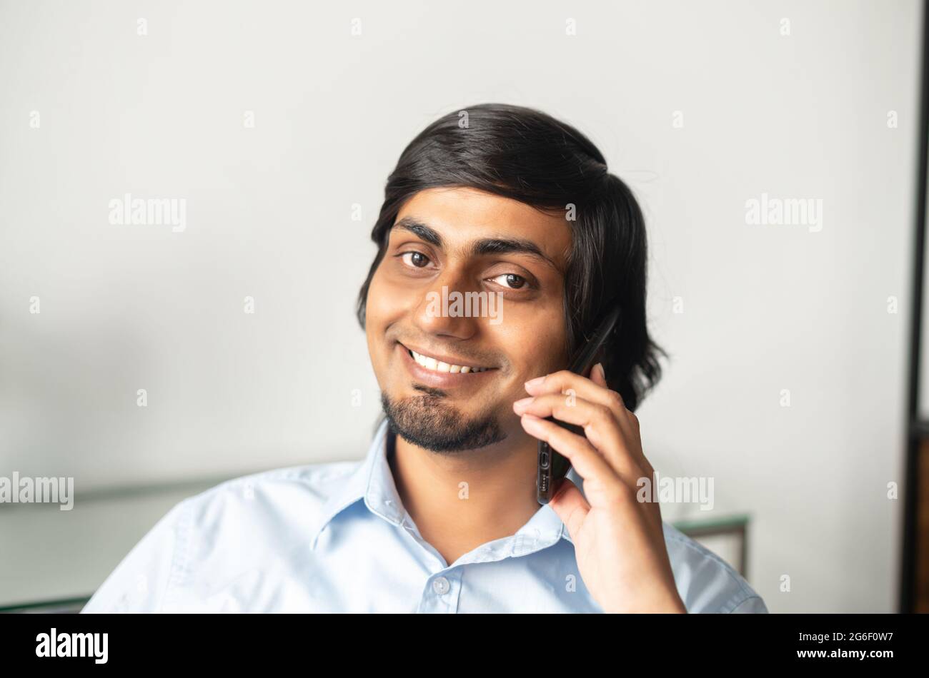 Prise de vue d'un homme d'affaires indien souriant dans une chemise élégante et décontractée parlant sur le smartphone et regarde la caméra, l'homme de l'est a une conversation téléphonique agréable Banque D'Images
