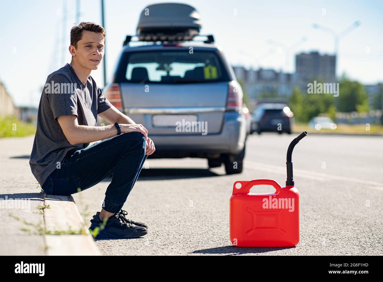 Une cartouche rouge sur l'asphalte près de la voiture. La voiture a manqué d'essence et a calé. Un jeune homme espérant obtenir de l'aide sur la route d'autres conducteurs Banque D'Images