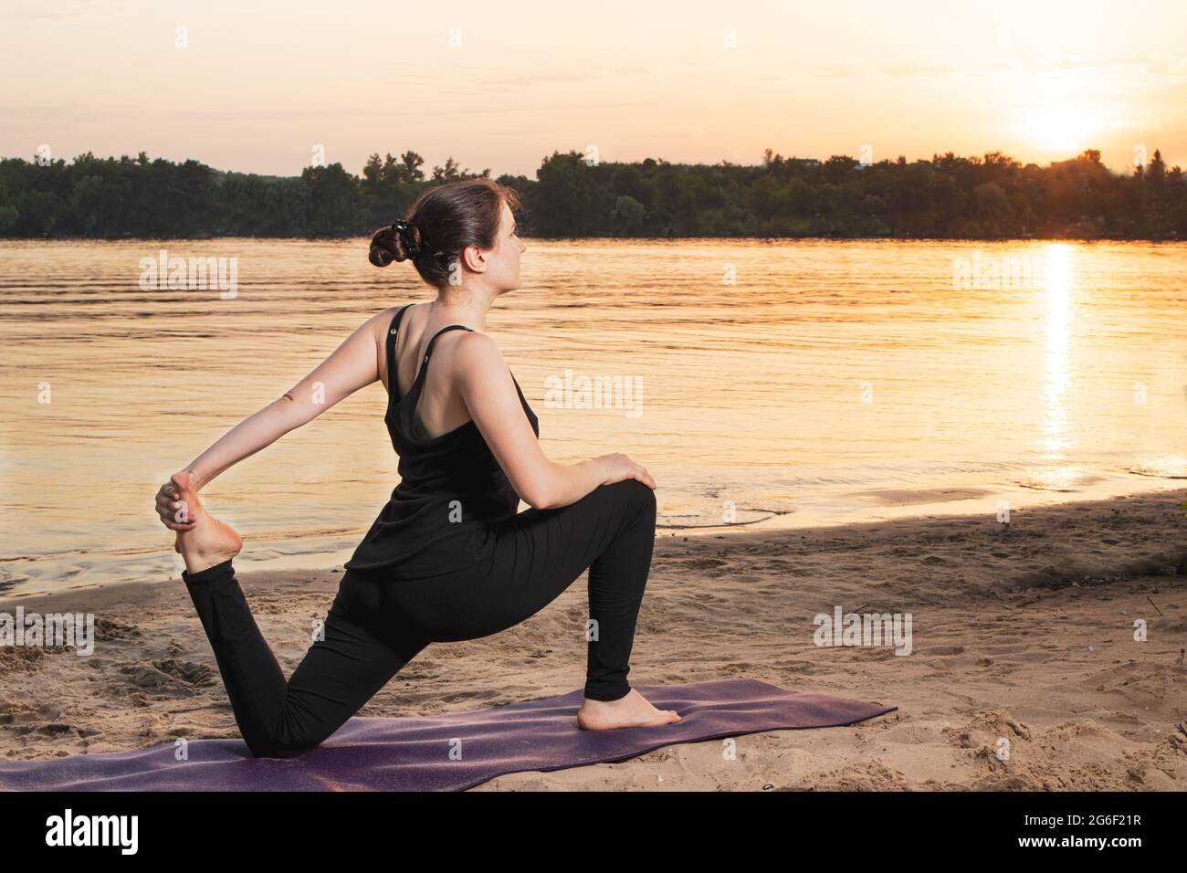 Une femme de sport pratique le yoga au coucher du soleil près de la rivière  sur la plage dans la nature. Étirant l'avant de la cuisse des quadriceps,  placez pour Photo Stock -
