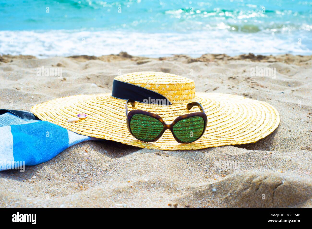 Accessoires de protection contre le soleil sur une plage de sable au bord de l'eau. Chapeau de paille avec ruban. Lunettes de soleil. Serviette en paréo de coton. Banque D'Images