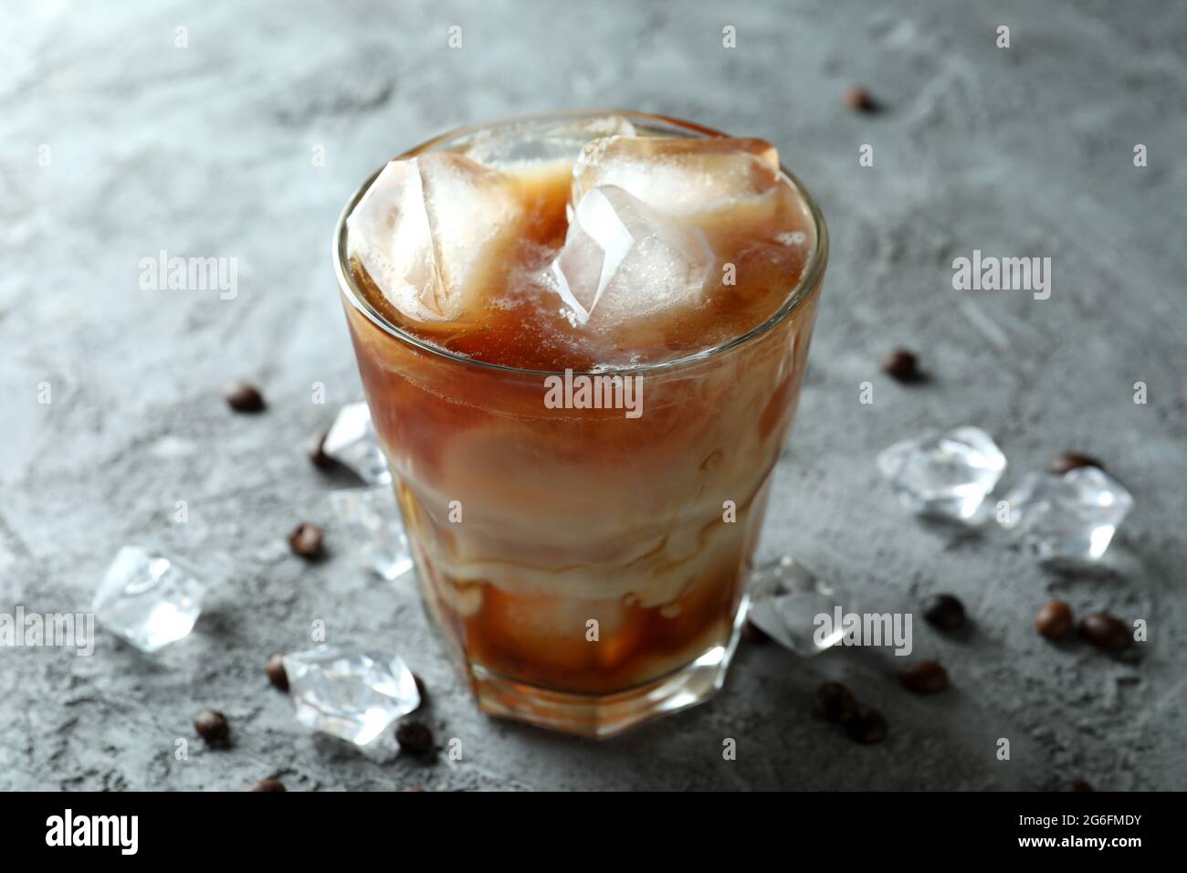 Un verre de café glacé, de haricots et de glace sur une table texturée grise Banque D'Images