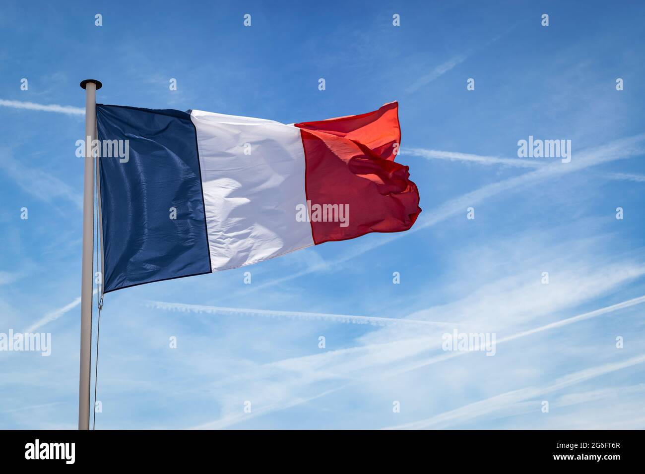 Le drapeau français sur le mât flotte dans le vent contre le ciel bleu. Banque D'Images