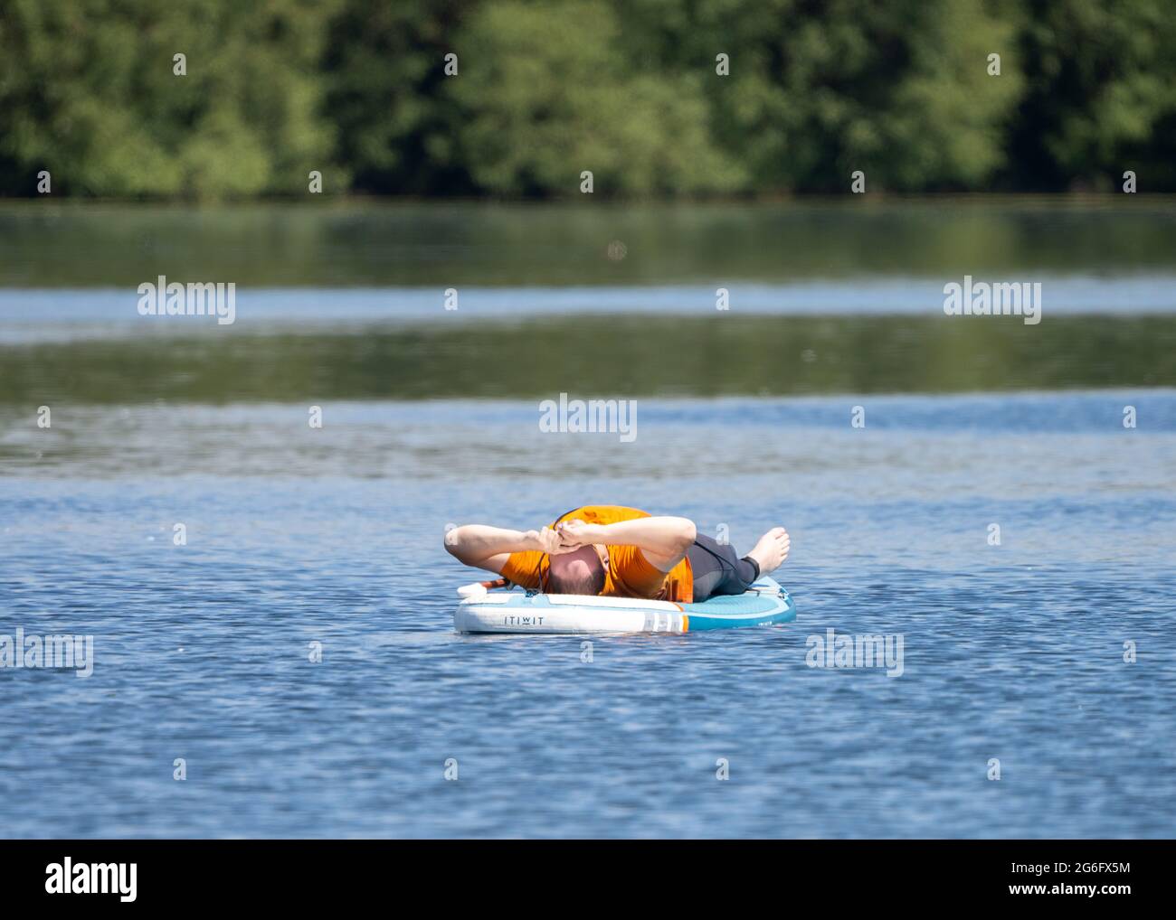 Homme anonyme endormi sur le plateau flottant flottant vers la mer dans le lac rapidement endormi. Bateau de surf gonflable sur l'eau calme. Banque D'Images