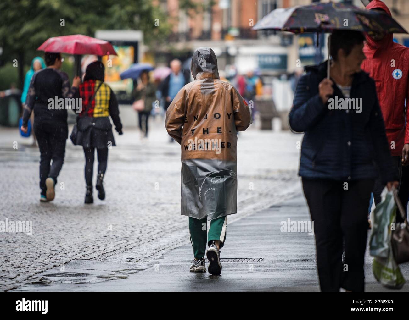 Profitez du manteau de pluie porté par les amateurs de shopping de rue dans le centre-ville sombre et humide. Parasols et temps d'été typiquement anglais Banque D'Images