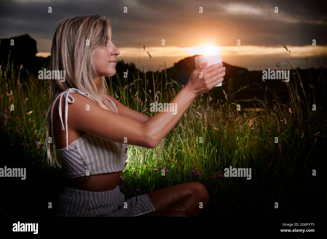 Fille blonde pratiquant la méditation au coucher du soleil avec une bougie Banque D'Images