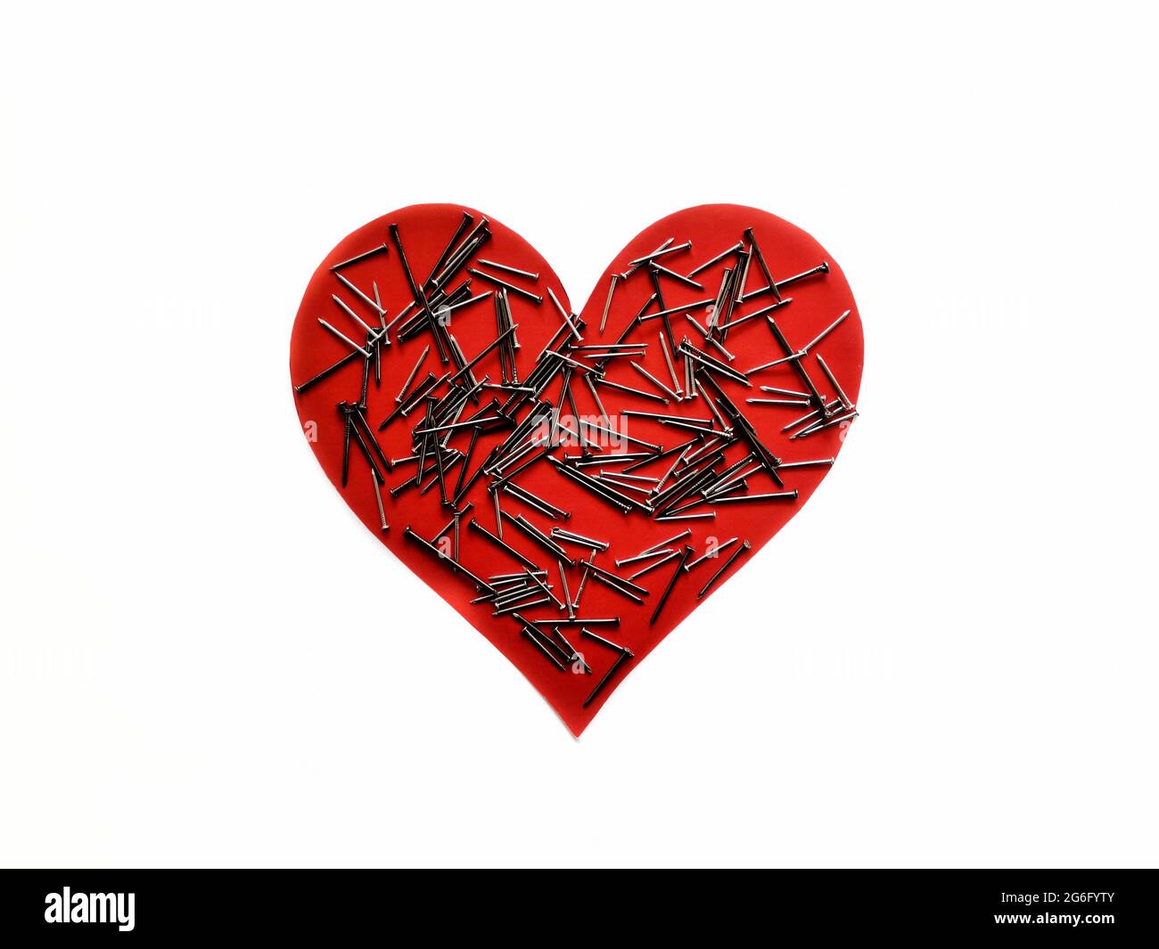 Coeur rouge et clous de couleur métal sur elle. Fond blanc, coeur rouge et ongles. Cœur souffrant. Banque D'Images