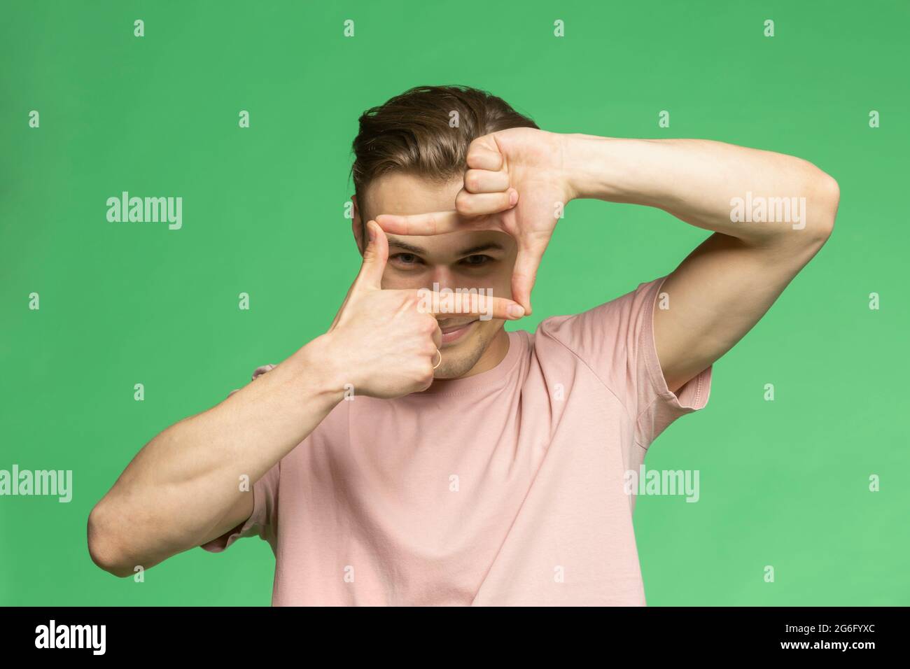 Studio portrait jeune homme gesturant cadre de doigt sur fond vert Banque D'Images