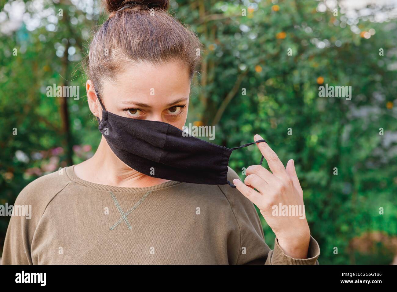 Bonne fille positive prend le masque médical de protection du visage à l'extérieur. Jeune femme qui retire le masque souriant après la vaccination. Pandémie de coronavirus Banque D'Images