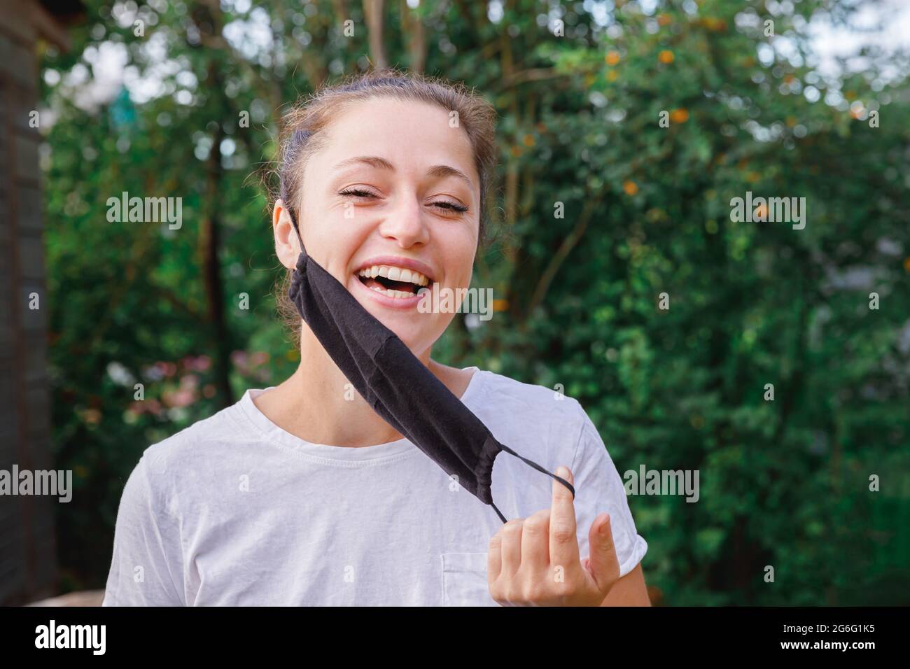 Bonne fille positive prend le masque médical de protection du visage à l'extérieur. Jeune femme qui retire le masque souriant après la vaccination. Pandémie de coronavirus Banque D'Images