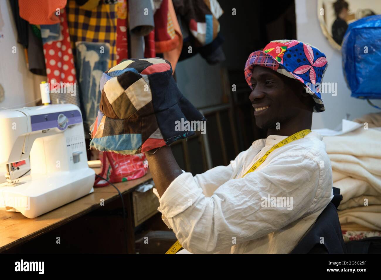 Tailleur noir souriant et examinant le chapeau qu'il fabrique dans une boutique de couture. Atelier de couture africain. Banque D'Images