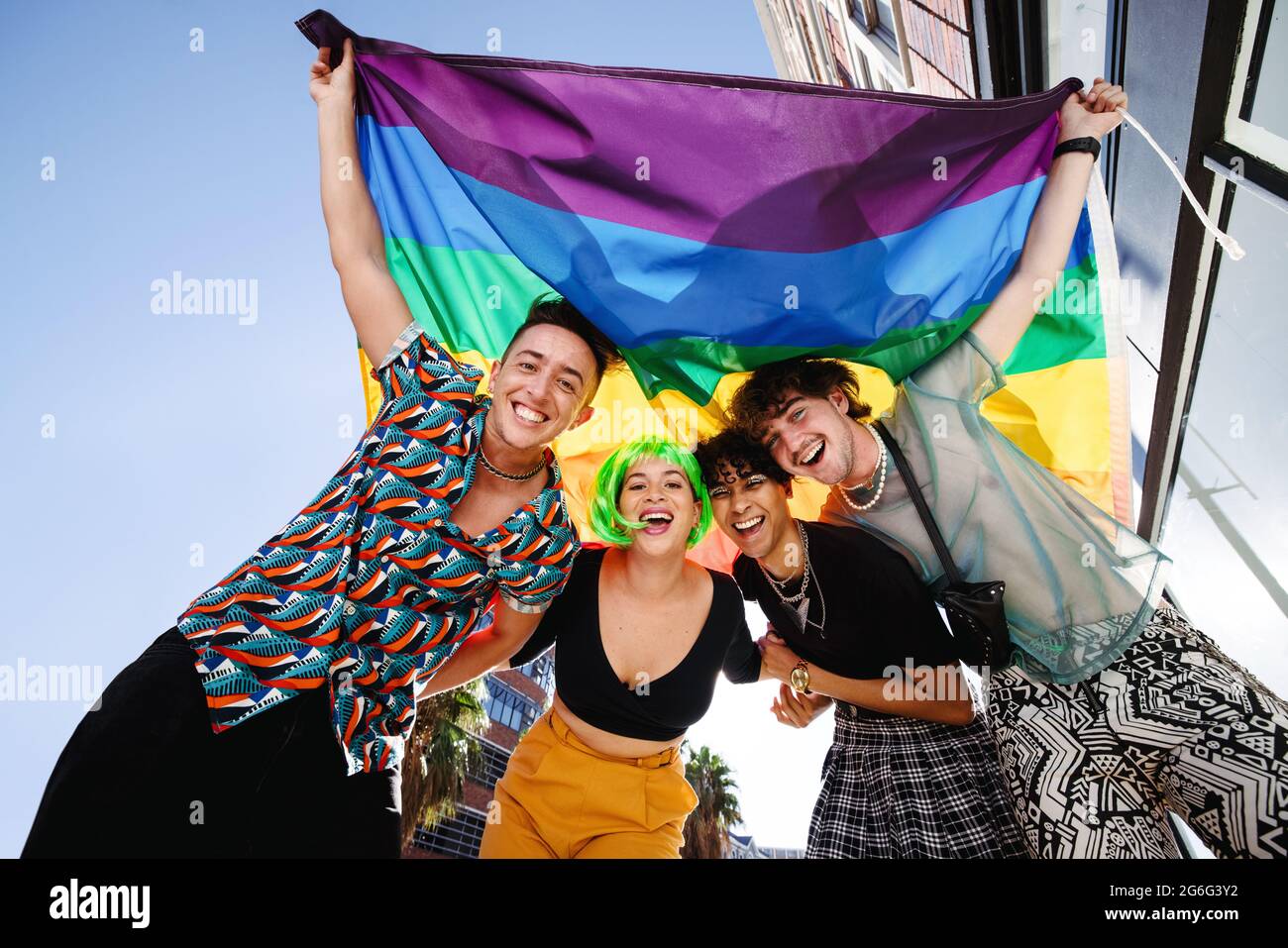 Quatre jeunes célèbrent leur identité queer lors d'un défilé de fierté gay. Groupe de jeunes LGBTQ+ souriant gaiement tout en élevant l'arc-en-ciel Banque D'Images