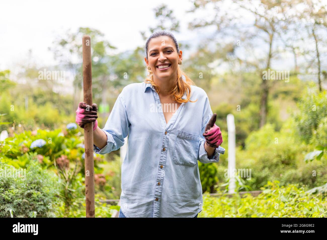 portrait d'une femme heureuse dans son jardin potager avec une pelle-bâton dans sa main Banque D'Images