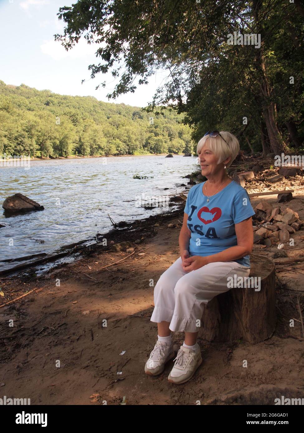 Belle femme blonde aux cheveux assis sur une souche le long du fleuve Delaware en Pennsylvanie tout en appréciant le paysage. Banque D'Images