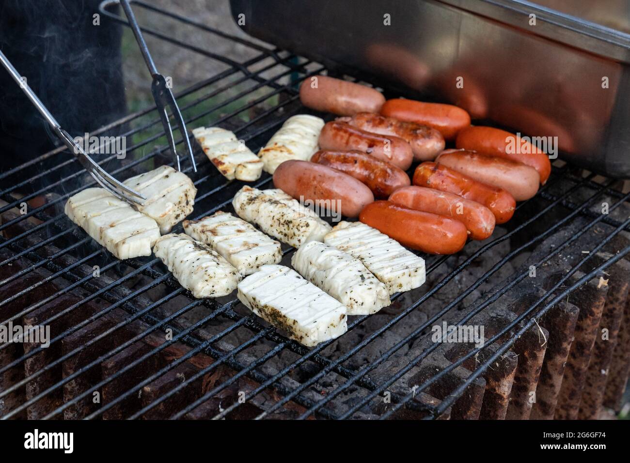 Avoir un barbecue avec des coals chauds dehors, la culture du fromage de haloumi avec des pinces sur un barbecue ou un barbecue. Banque D'Images