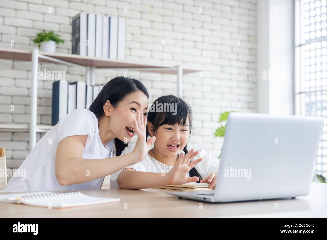 La mère asiatique enseigne les devoirs à la fille sur un ordinateur portable à la maison, famille heureuse et éducation concept d'école à domicile, la mère et la fille vague main pour accueillir le professeur Banque D'Images