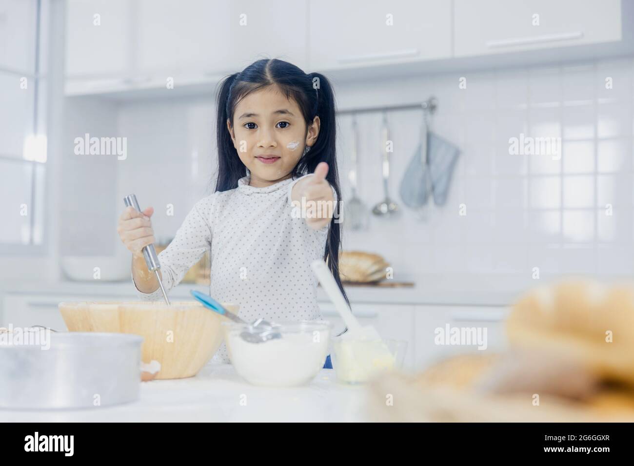 Bonne et amusante jeune fille asiatique apprendre à cuisiner sucré ou de boulangerie et de montrer thump up Banque D'Images