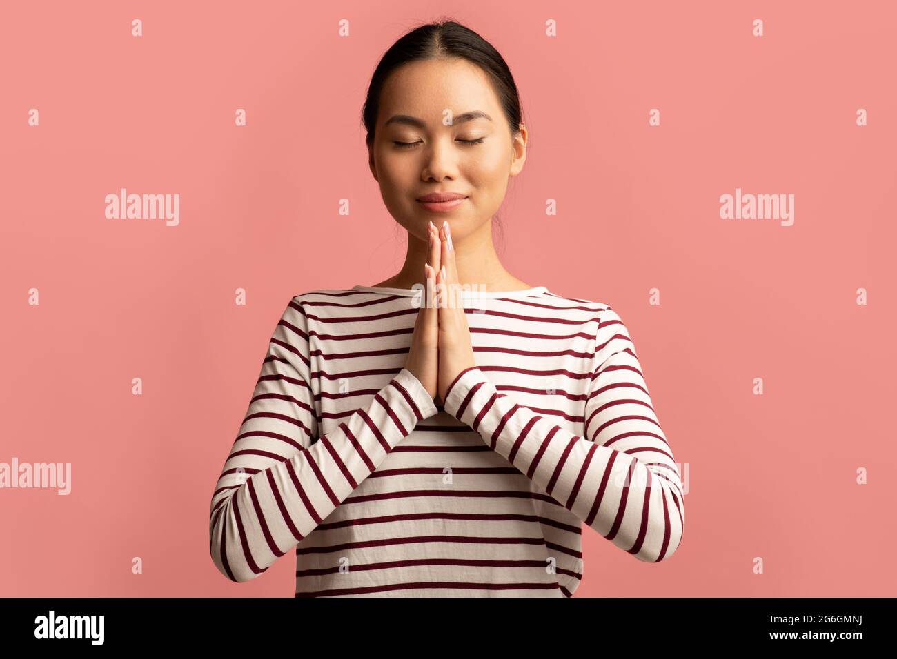 Portrait de la jeune femme asiatique qui priait avec les mains claspées près du visage Banque D'Images