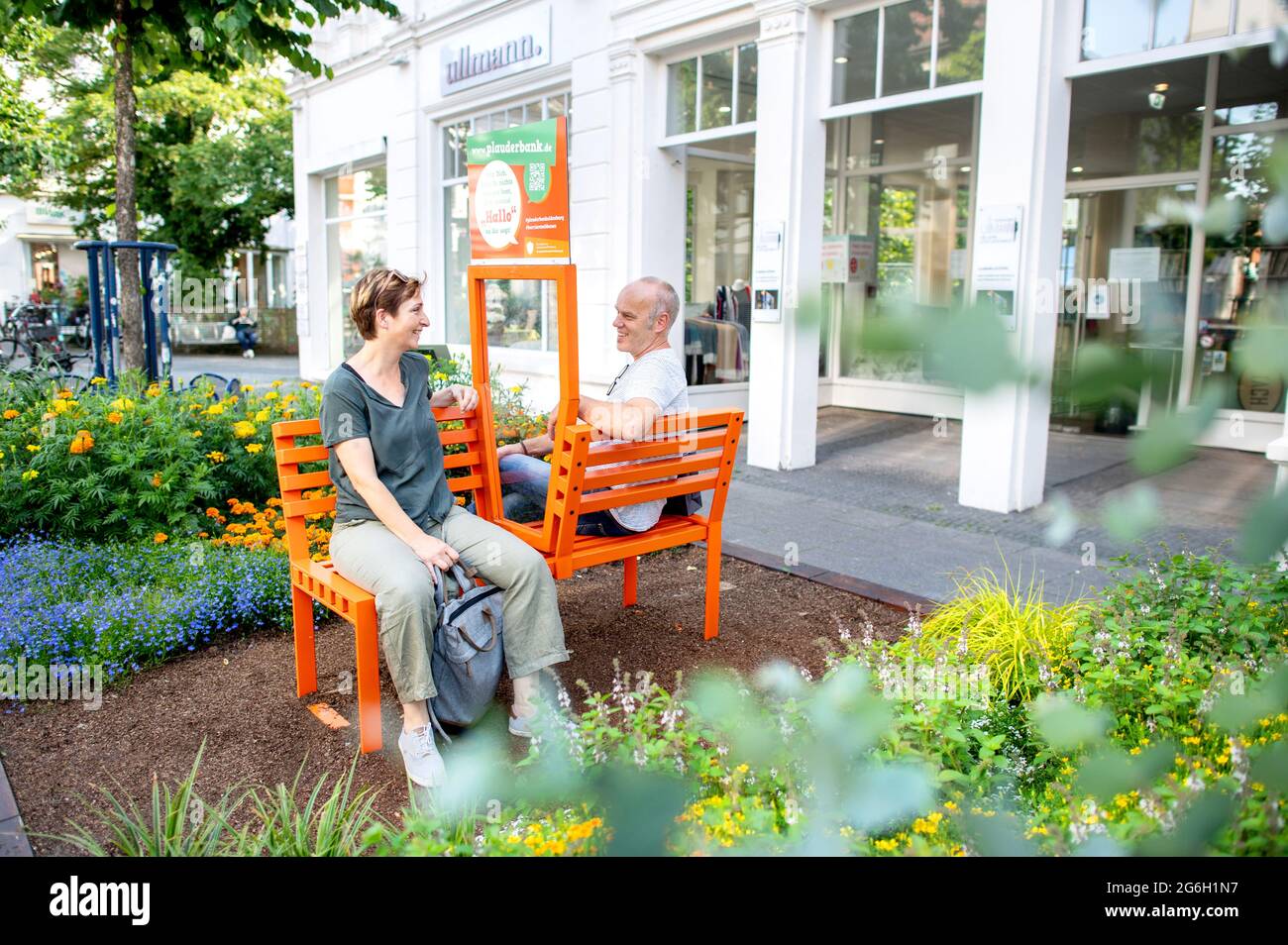 03 juillet 2021, Basse-Saxe, Oldenburg: Doris et Ansgar d'Ochtrup s'assoient sur un banc de chat dans le centre-ville d'Oldenburg. Les bancs corona-conformes sont équipés d'un panneau de verre entre les sièges et sont destinés à inviter les gens à engager la conversation avec les autres. Depuis mai, dix bancs de chat ont déjà été installés à divers endroits de la ville. Photo: Hauke-Christian Dittrich/dpa Banque D'Images