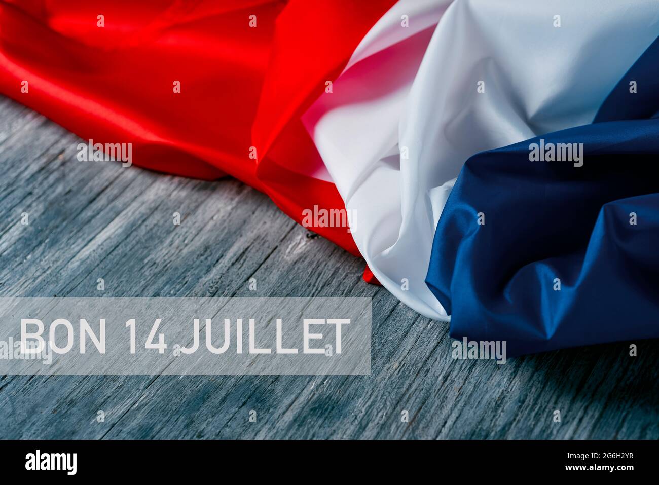le texte bon 14 juillet, heureux 14 juillet, la journée nationale de france écrite en français, et un drapeau français sur fond de bois rustique gris Banque D'Images