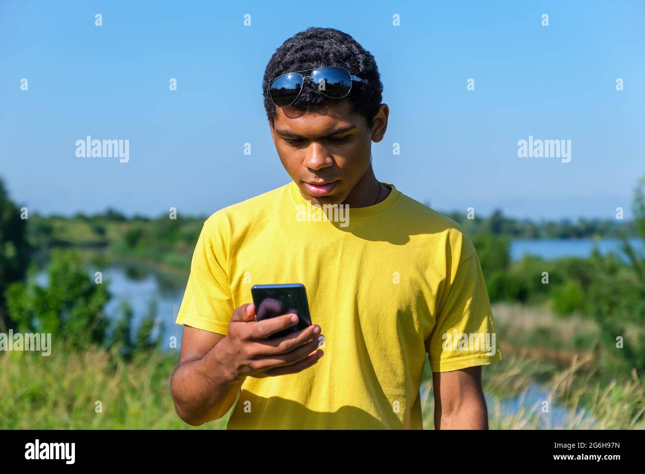 Un type afro-américain utilise le téléphone, les appels et les discussions en ligne à l'extérieur près de la rivière Banque D'Images