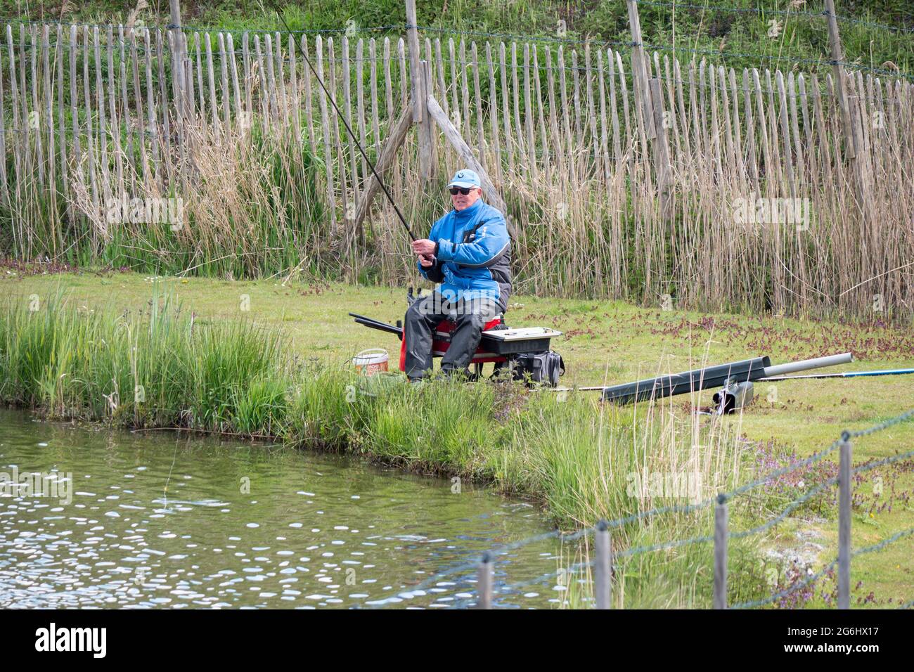 Kruibeke, Belgique, le 25 mai 2021, un pêcheur avec une veste bleue de casquette pêche est une canne sur un étang Banque D'Images