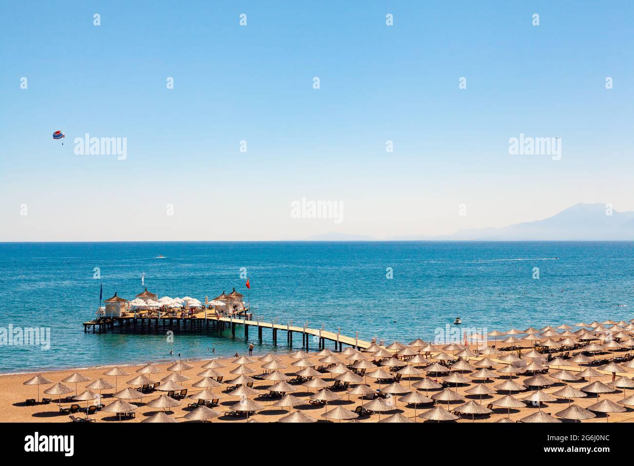 Les personnes se baignant, se bronzer ou faire d'autres activités sur la plage. Grand groupe de parasols en paille sur le sable. Les personnes bronzant sur un quai en bois et Banque D'Images