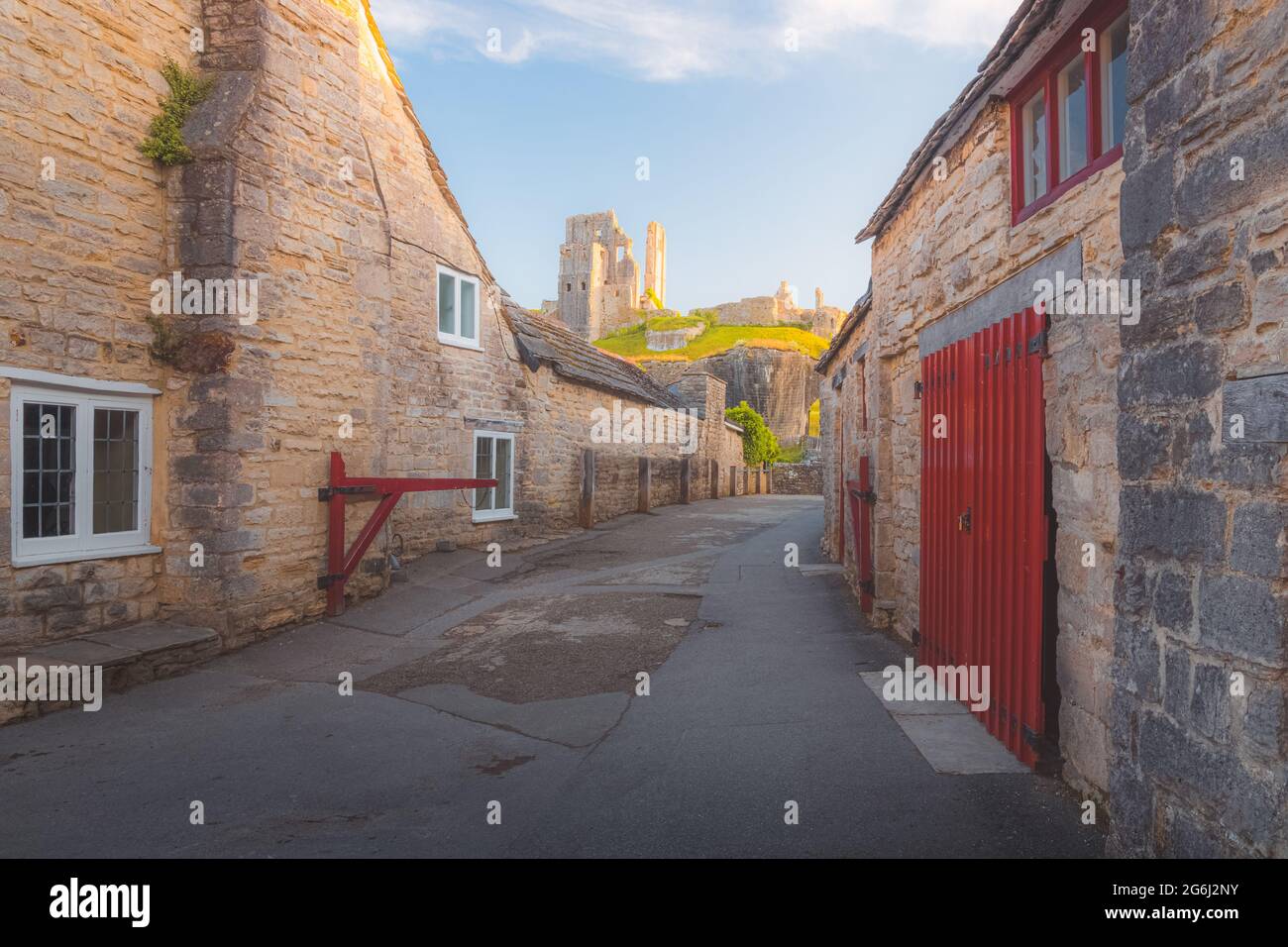Les ruines médiévales au sommet d'une colline dans le village pittoresque et historique de Corfe Castle, Dorset, Angleterre avec coucher de soleil à l'heure d'or ou lever de soleil lumière d'été. Banque D'Images