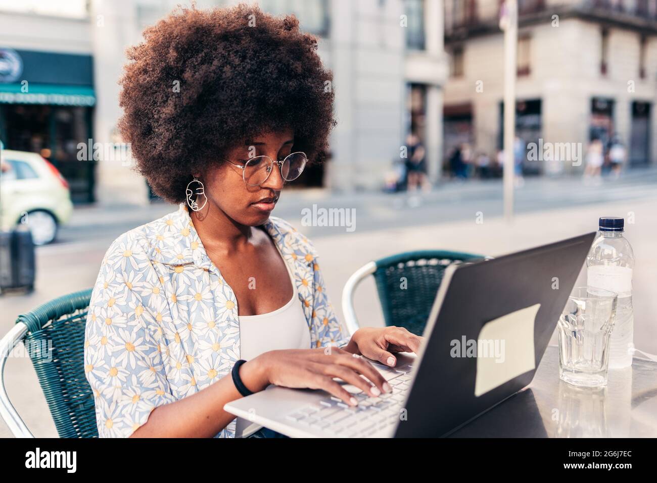 femme afro assise sur une terrasse de bar et utilisant un ordinateur portable. Concept de travail à distance d'une cafétéria Banque D'Images