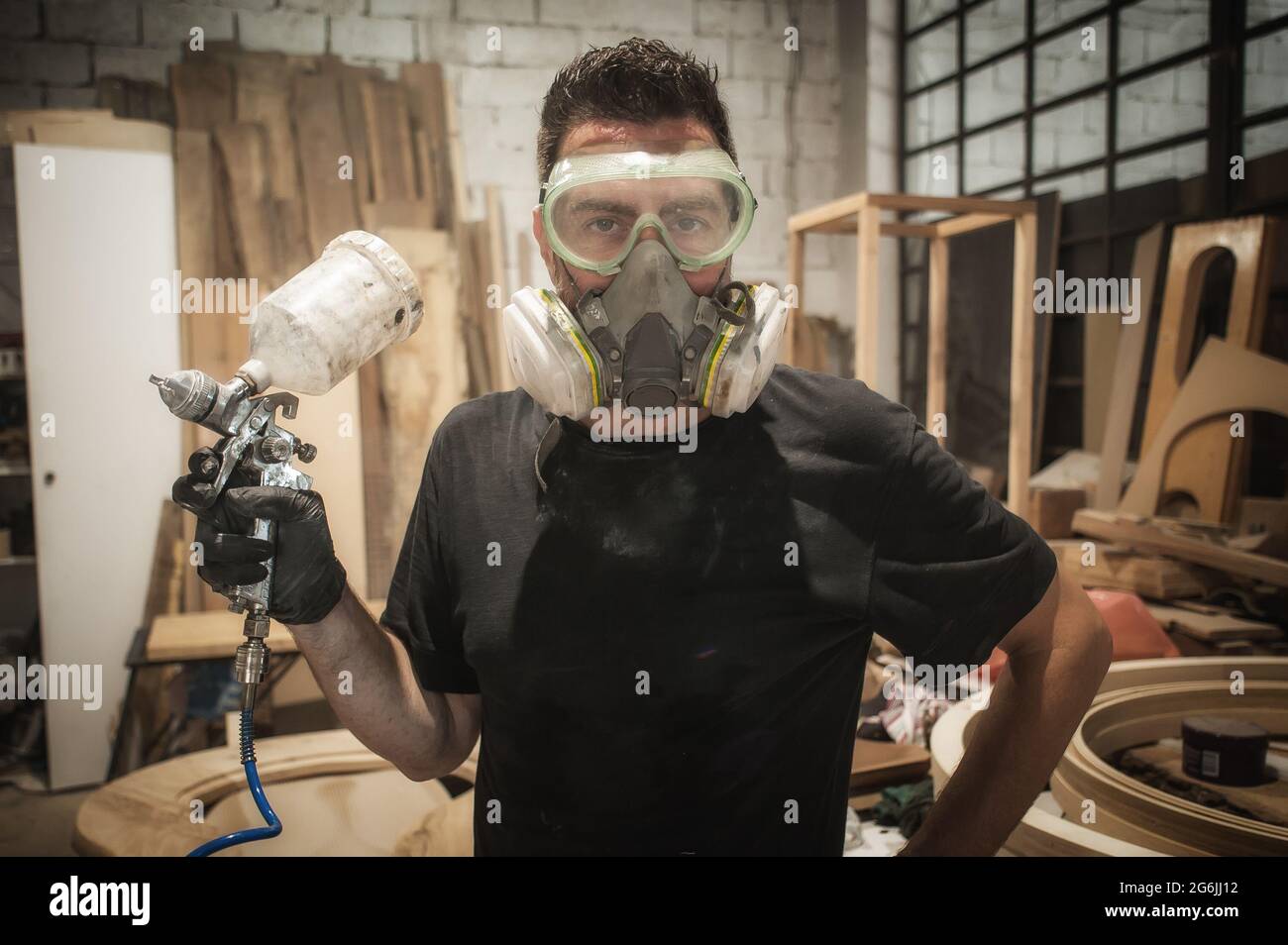 Travailleur drôle. Un ouvrier fait de la comédie et pose avec du vernis de peinture à la brosse à air dans l'atelier Banque D'Images