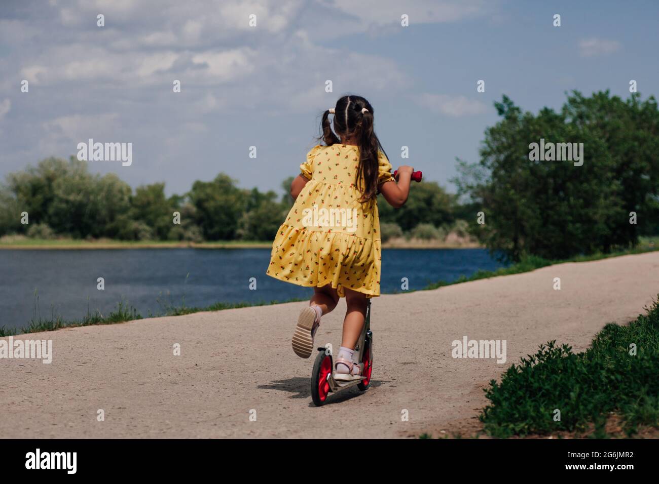 portrait de style de vie vue arrière d'une fille dans une robe jaune à cheval sur un scooter sur la rive de la rivière en été, une fille apprenant à monter un scooter Banque D'Images