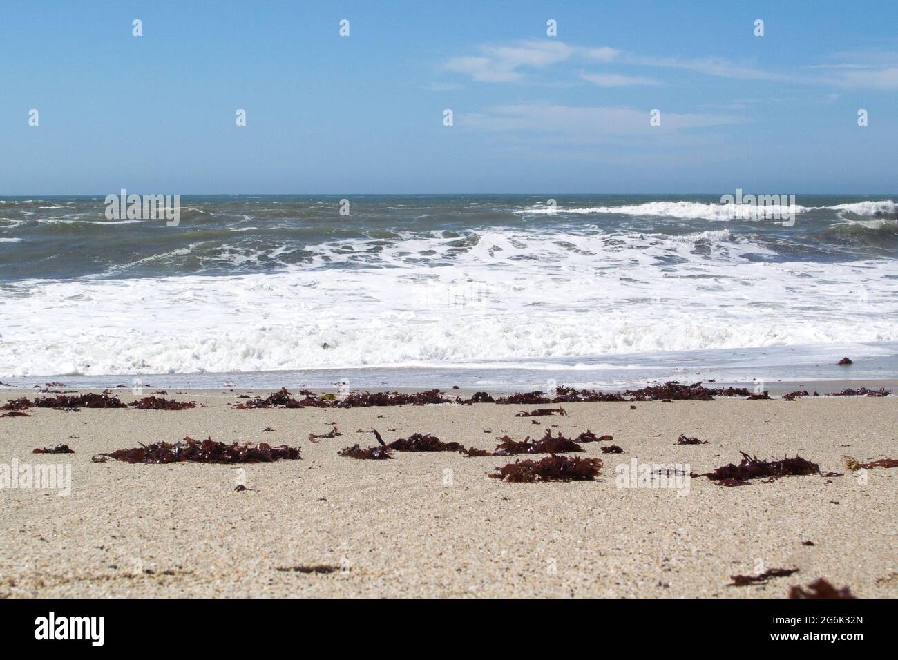Ciel, Océan et Shore shone que trois stips horizontaux, vagues moussant, l'herbe de mer rouge lavé sur la plage de sable. Banque D'Images