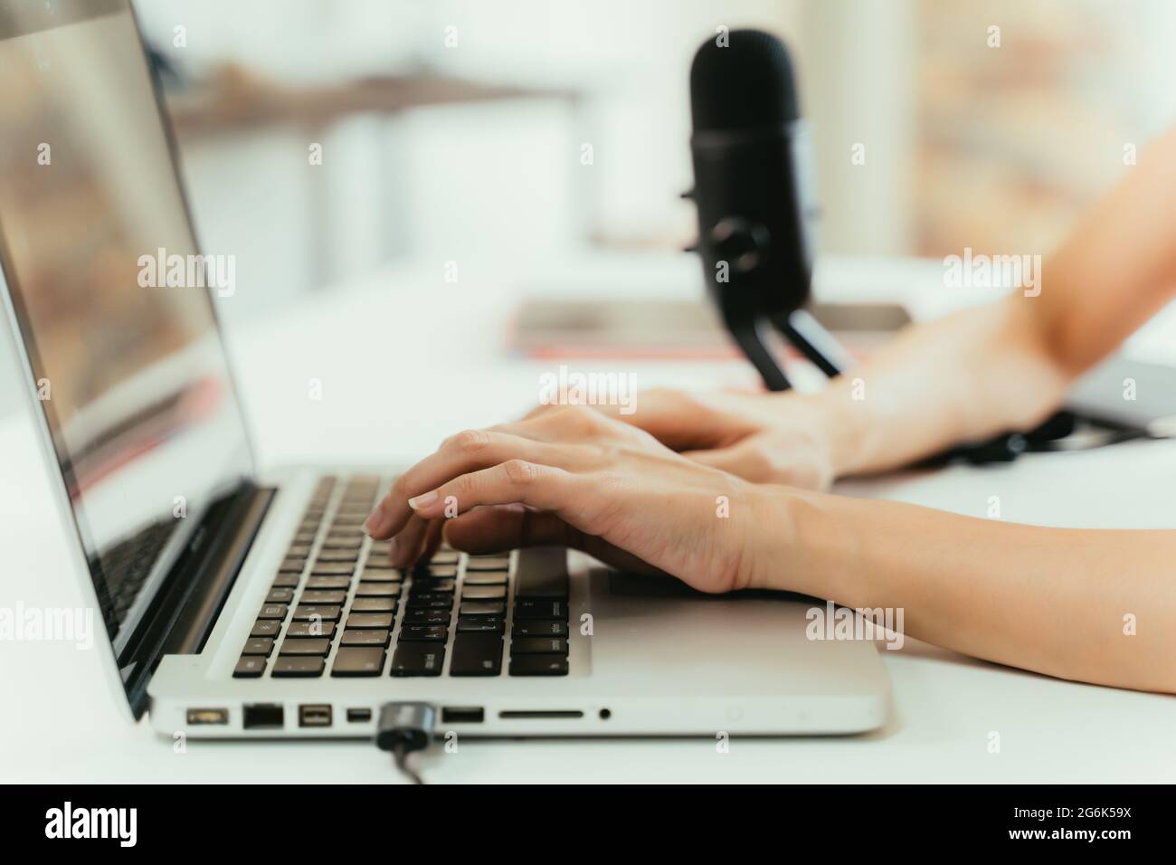 Gros plan des mains de jeunes femmes podcaster écrivant un nouveau blog pour les médias sociaux tout en tapant sur un ordinateur portable sur le bureau avec un micro en arrière-plan à la maison Banque D'Images